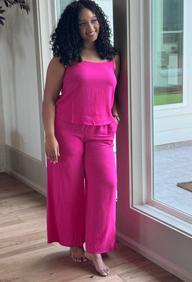 Woman wearing a bright pink outfit standing in a room with wooden flooring and a large window.